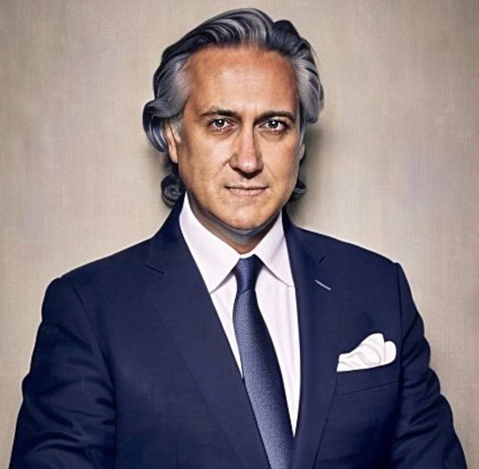 Formal portrait of a middle-aged man with gray hair wearing a dark navy suit, white dress shirt, and dark tie with white pocket square