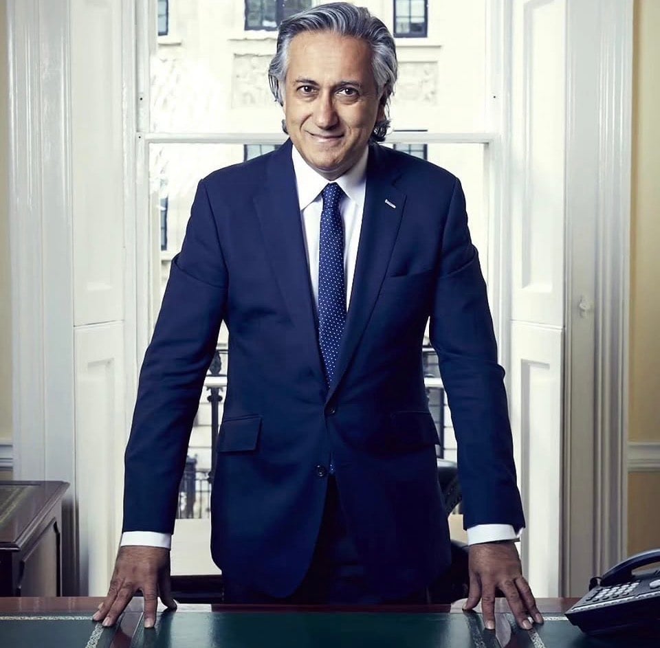 Professional man in navy suit and polka dot tie standing at desk in formal office setting with white columns